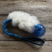 Hälge är en hundleksak med blå boll och blått expanderhandtag. Vitt svenskt fårskinn.